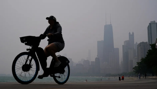 　27日，在芝加哥，天际线被加拿大野火雾霾笼罩，一人骑自行车沿着密歇根湖畔行驶。图源：美联社