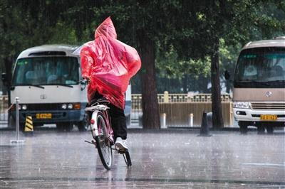 昨日上午，北京西单附近，市民雨中边骑车边整理雨衣。新京报实习生 陈婉婷 摄