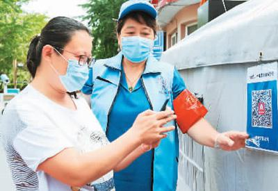 在北京市首都师范大学社区出入口，疫情防控志愿者宋春娟（右）指导进入社区人员扫描健康宝二维码。新华社记者 任 超摄