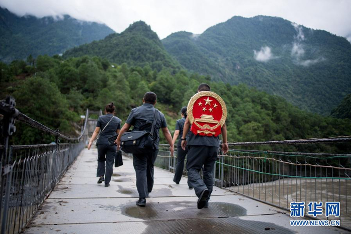 云南省怒江傈僳族自治州贡山县人民法院法官邓兴背着国徽与同事们跨过怒江（2019年8月30日摄）。为方便居住在高山峡谷里的农村群众，邓兴和同事们一起背着国徽，组建巡回法庭。每年足迹遍及50多个村镇，行程近万公里。新华社记者 江文耀 摄
