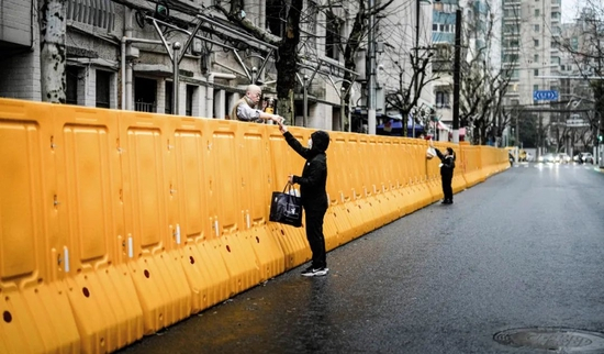 　2022年3月25日，上海一处封控区，人们隔着护栏交接食物等。图/澎湃影像