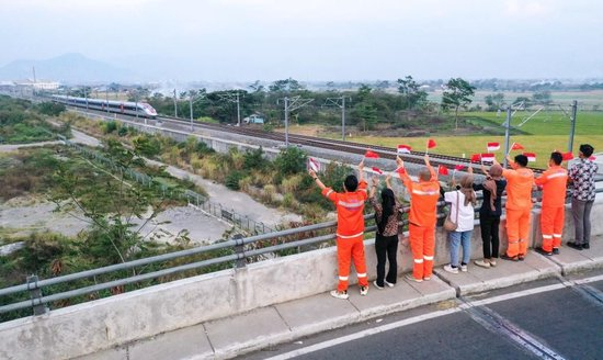 10月17日，在印度尼西亚万隆一座天桥上，雅万高铁建设单位之一中铁电气化局的中国和印尼籍员工挥舞着中国和印尼两国国旗，向远处驶来的一列雅万高铁高速动车组列车欢呼（无人机照片）。新华社记者徐钦摄