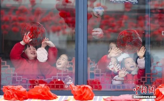  资料图：幼儿园内，小朋友们在老师的指导下贴窗花。