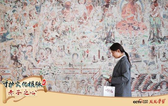 2023年4月25日，敦煌研究院文物数字化保护团队创意营销人员从一幅高保真复制壁画前走过。