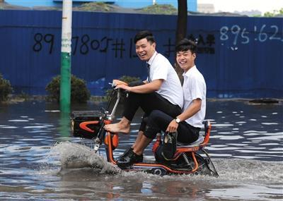 6月23日，受大雨影响燕郊创意古街中段积水深约25公分，两名男子骑电动车通过约500米积水路段。 新京报记者 王飞 摄