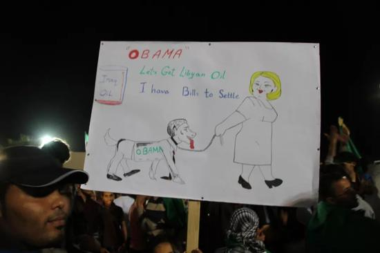 　　2011年4月，在的黎波里的阿齐齐亚兵营，卡扎菲支持者举出反美漫画。（谷子地佩刀2011年4月摄于的黎波里）