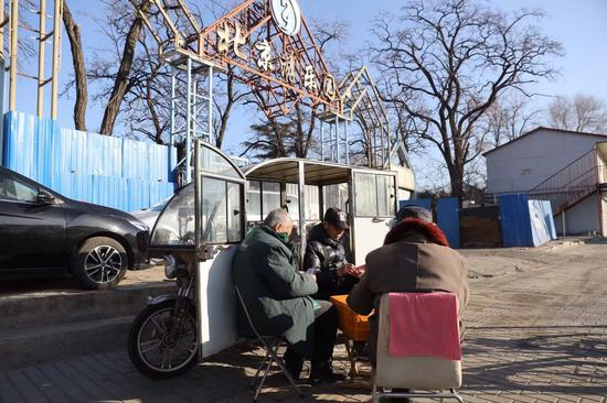 12月17日，原北京游乐园南门，大门已经被封挡，几位老人在晒太阳打牌。新京报记者 王贵彬 摄