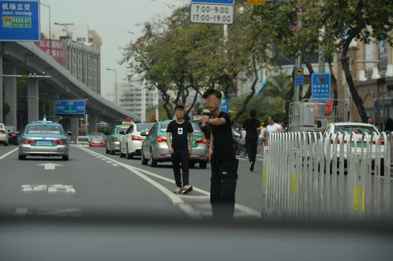 　　3月17日下午，广州市白云世界皮具贸易中心门前的解放北路，一名拉客人员在机动车道上往一辆私家车内递名片。 新京报记者 吴江 摄