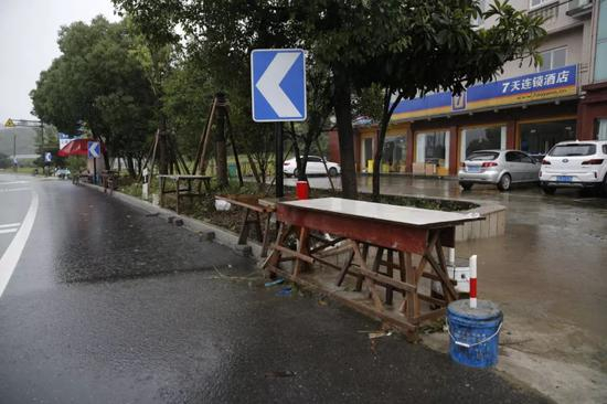 　　7月13日，章子欣爷爷原来卖水果的摊位，背后是梁某华和谢某芳曾住过的连锁酒店。新京报记者 侯少卿 摄