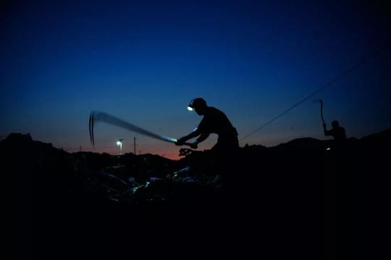 戴上矿灯，背着篓筐，在夜里就开始“淘金”的拾荒人。 　　图/视觉中国