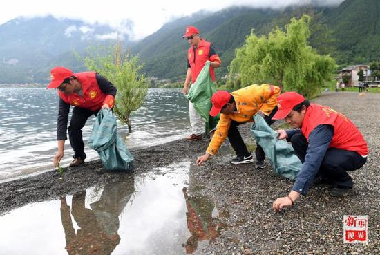 ↑次里平措（右二）和几名村民在泸沽湖边捡拾垃圾和杂物。新华社记者蔺以光摄