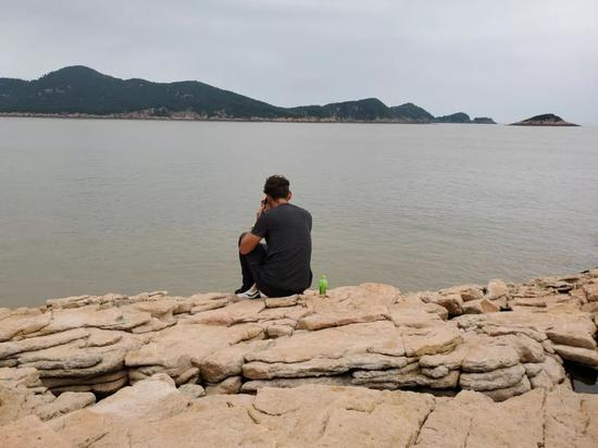 7月11日，章军坐在海边岩石上，焦急地等待救援队的进展。新京报记者 李云蝶 摄
