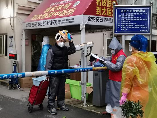 江码社区滨江苑小区门口，居民们正排队领取生活物资，一旁的社区工作人员正在进行记录。