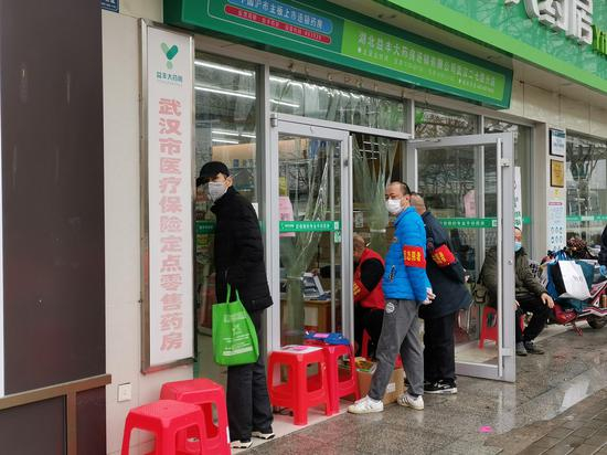 江码社区附近的一家药房门外，好几名社区工作人员或志愿者正等着排号为居民买药。