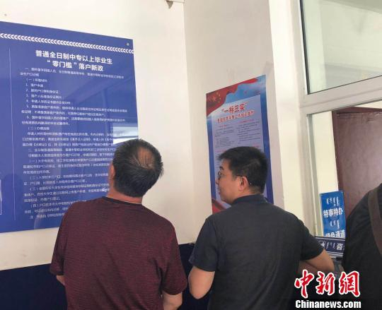 　　图为呼和浩特市新城区东风路派出所中，前来办理户籍登记的市民被墙上的“落户新政”吸引。　陈峰　摄