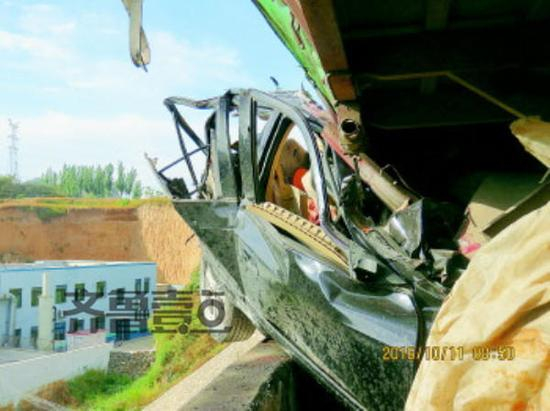 被挤压在大货底部的轿车严重变形，车内2人却毫发无损。