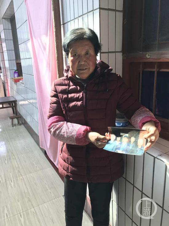 图为王琪弟媳拿着老家兄弟姐妹合影照片
