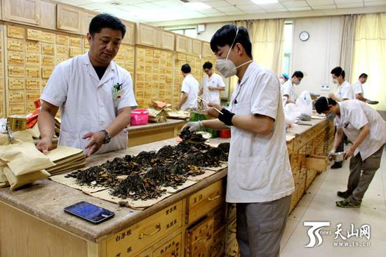  自治区中医医院中药房，工作人员使用电子终端完成中药的分拣工作。
