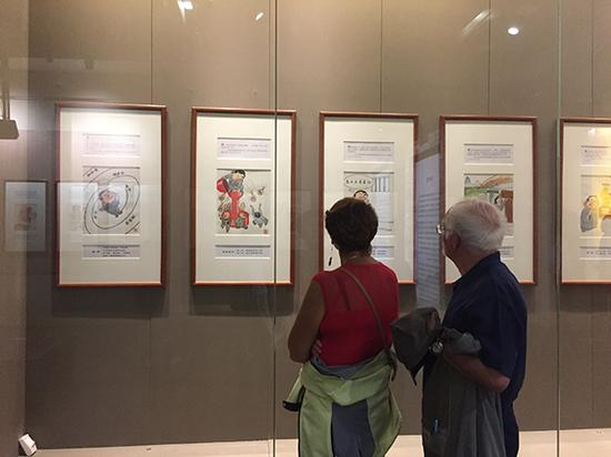 漫展吸引了两位外国游客，一旁有导游向他们解释漫画主题。