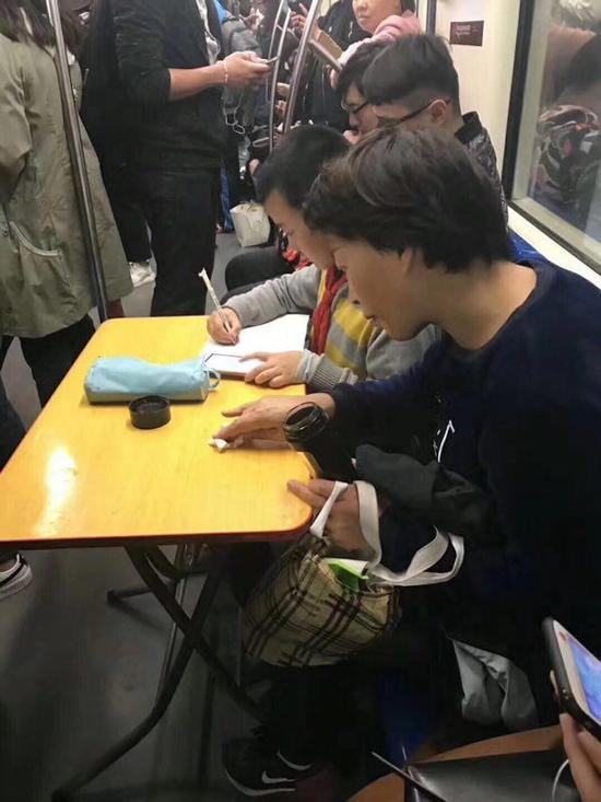 11月6日，上海地铁8号线，在家长陪同下，孩子在车厢内摊开折叠桌写作业。 网友供图