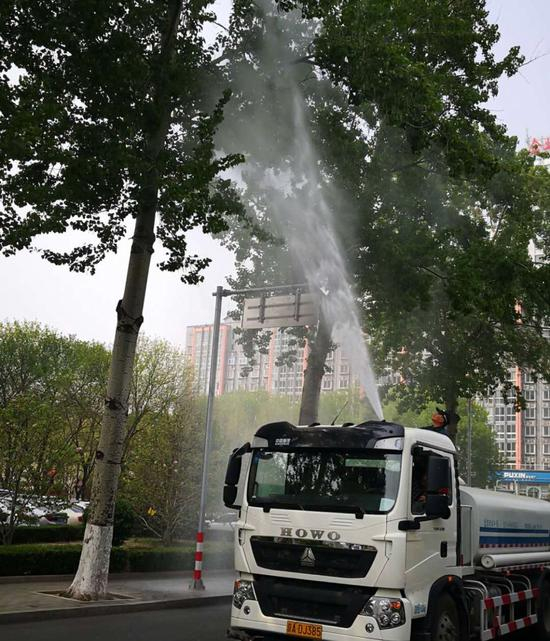 对道路两旁的杨树，园林工人使用高压水枪冲洗树冠，以解决当下的飞絮烦恼。