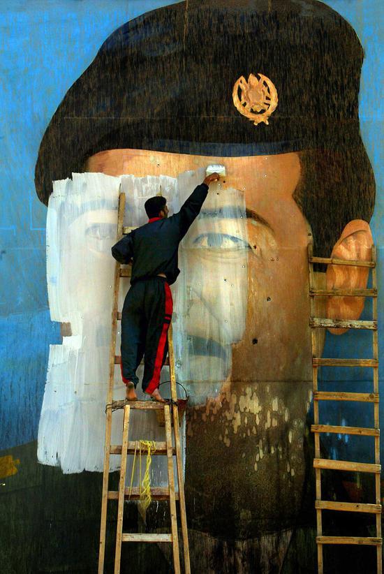 　　布满弹坑的墙上，Salem Yuel在萨达姆肖像上作画。美国军队到达并控制巴格达之后，关于萨达姆的标志很快便消失了。卡罗林·科尔摄于伊拉克巴格达，2003年4月。图片来源：Carolyn Cole/Los Angeles Times