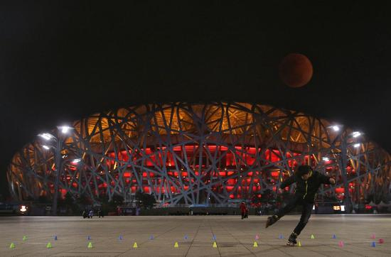 ▲21：20，鸟巢，一位游客在广场溜旱冰，一轮“血月”挂在半空。（图为二次曝光） 图/新京报网