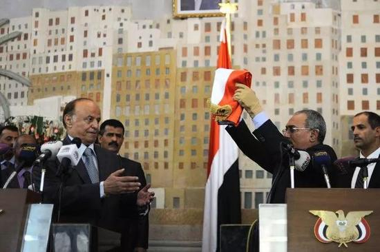 ▲2012年，萨利赫向也门新总统哈迪移交国旗。图据《纽约时报》