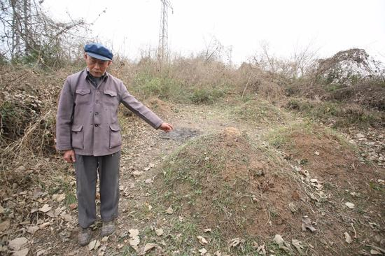 ▲幸存者梅寿芳的10位亲人被日军杀害。图为他指认埋葬10位亲人的墓地 。