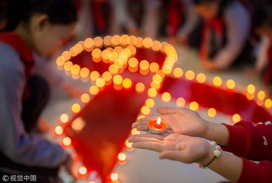 　　2017年12月1日，呼和浩特市玉泉区石头巷小学学生用蜡烛点亮红丝带，纪念世界艾滋病日。图片来自视觉中国
