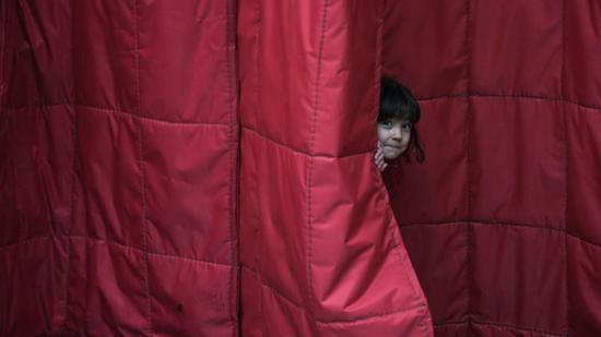 在大巴扎，一位维吾尔族小姑娘害羞的通过门帘打量着拿着摄影师。苏泽朗/摄