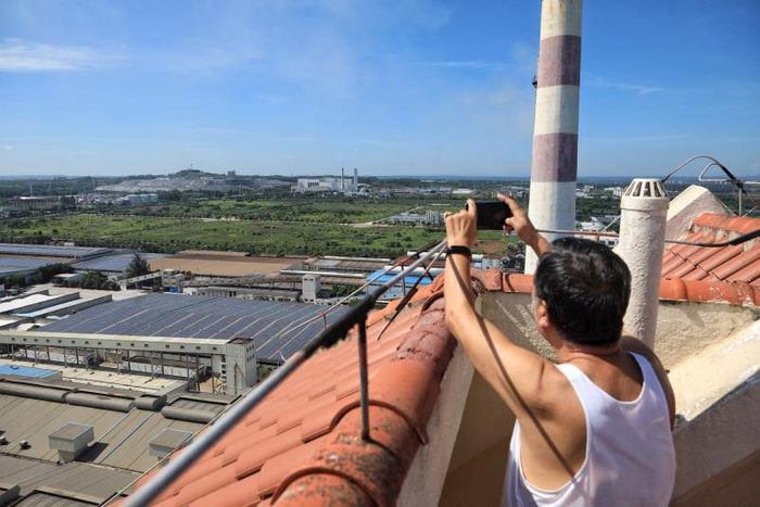  6月19日，海南省澄迈县，藏龙福地小区，一业主在顶楼用手机拍摄小区旁边的工厂和不远处的垃圾填埋场，这里离垃圾填埋场直线距离1公里左右。海南澄迈，居民抗议垃圾填埋场，焚烧厂。新京报记者 王嘉宁 摄