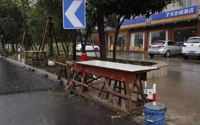 　　7月13日，章子欣爷爷原来卖水果的摊位，背后是梁某华和谢某芳曾住过的连锁酒店。新京报记者 侯少卿 摄