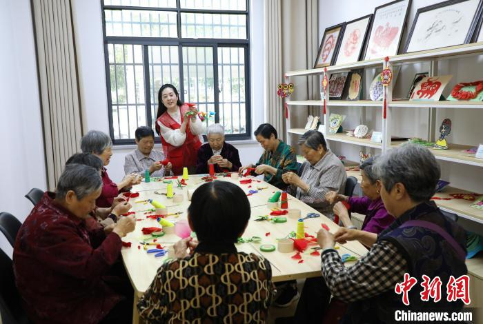在肥西县上派镇古埂社区综合性老年活动中心内,志愿者和老人一起制作