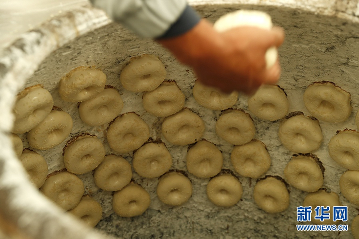 　　制馕师傅正在把馕坯放进馕坑烤制。新华网记者 焦鹏 摄