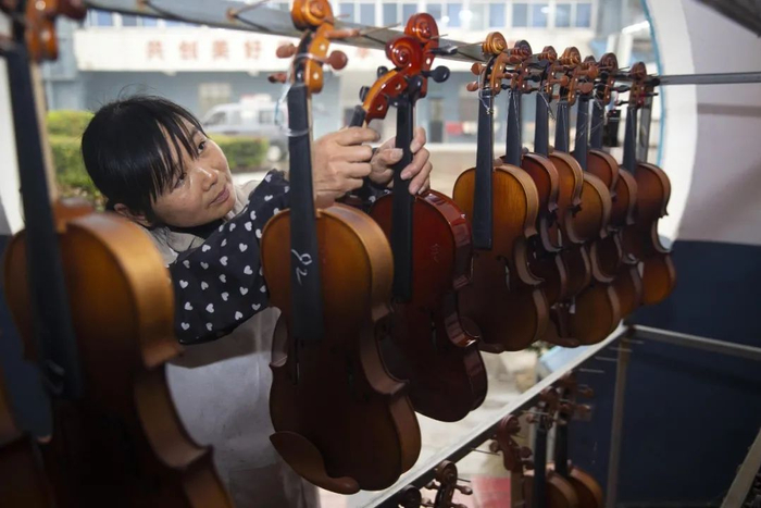 ▲2019年12月17日，在江苏泰州黄桥镇凤灵乐器集团，工人对小提琴成品进行质量检测。图/视觉中国