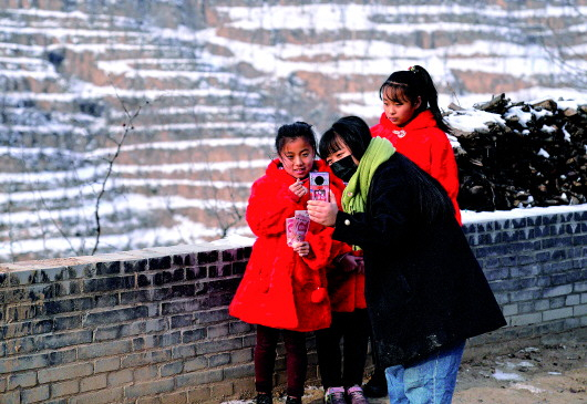 　在山西省吕梁市临县裴家局村，“格格”刘慧敏（中）在通过手机视频让穿上新衣服的孩子们和捐助衣物的爱心人士交流（11月30日摄）。本报记者牟宇摄