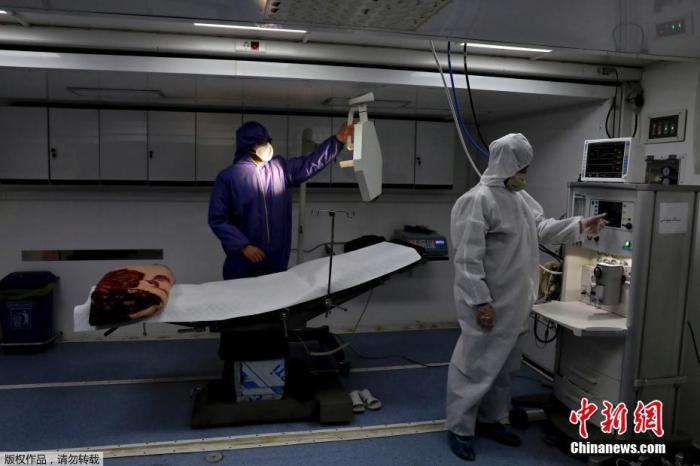 资料图：2020年3月，伊朗德黑兰国际展览中心，穿防护服的工作人员在操作医疗设备。