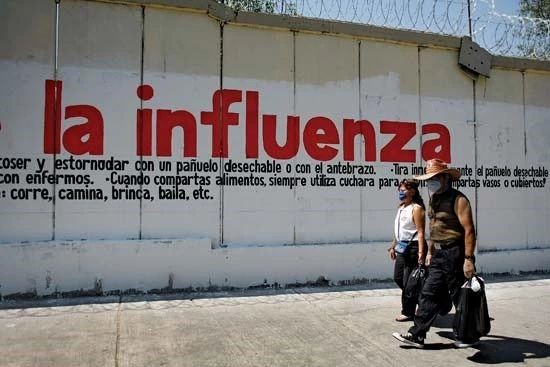2009年，墨西哥城，戴着防护性外科口罩的民众走过甲型H1N1流感警告标志。