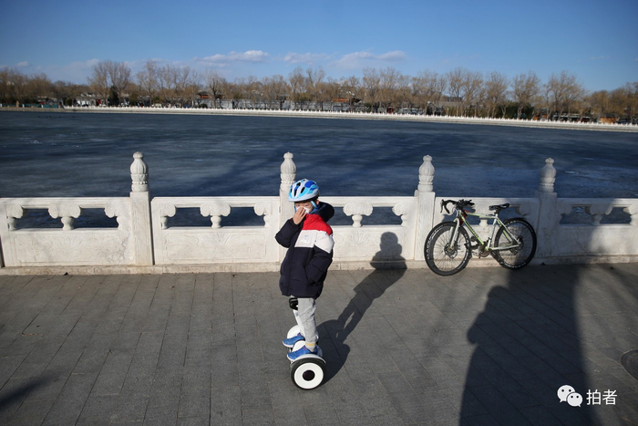 △ 3月1日，一个小男孩戴着口罩在什刹海边骑电动平衡车。摄影/新京报记者薛珺