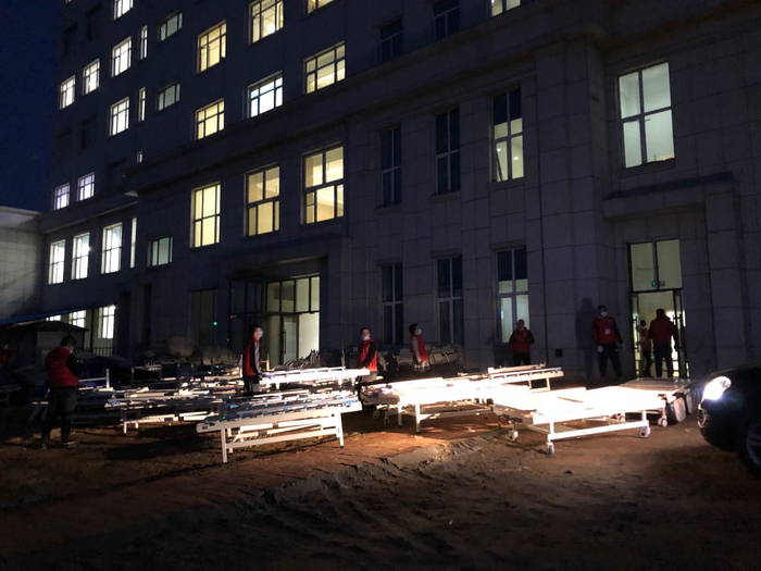  4月10日傍晚，穿着红马甲的志愿者，正在向建筑内搬抬医疗用床。