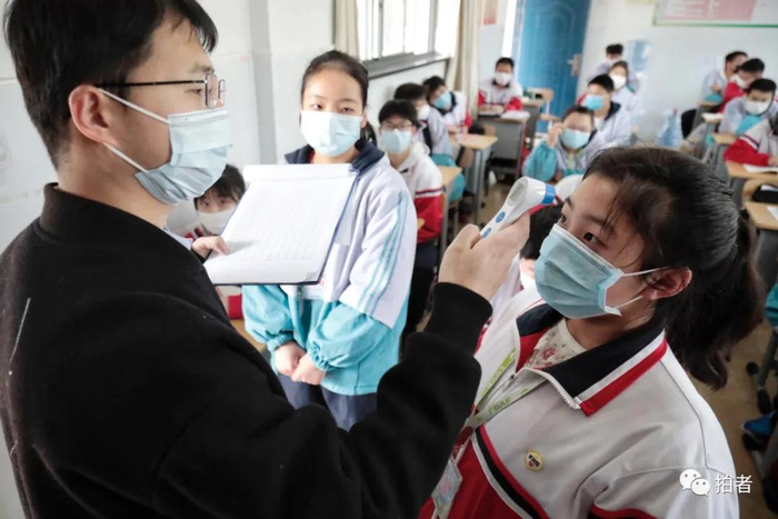 △ 教室内，老师为学生测体温并进行登记。