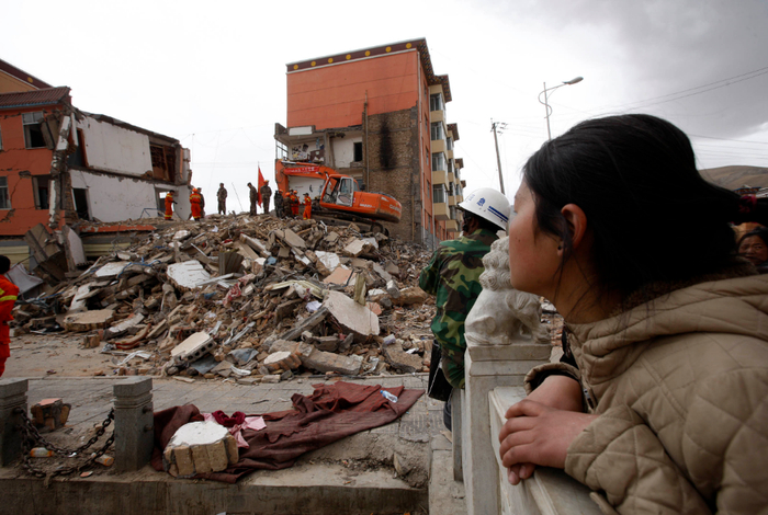 　　2010年4月17日，在青海玉树经营灯具生意的安徽人王群群，望着搜救队员在废墟上搜寻她的父亲王殿美。新华社记者 沈伯韩摄