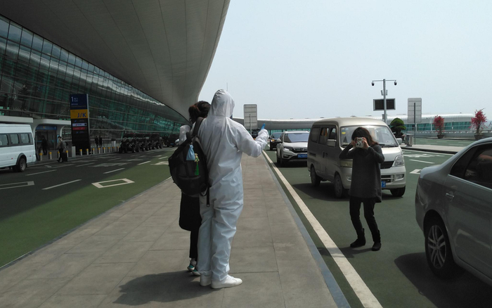  4月8日，武汉天河机场内，一位身着防护服的乘客在航站楼前与家人合影留念。新京报记者 海阳 摄