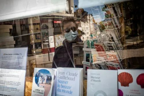 ▲4月26日，在法国巴黎，一名戴口罩男子的身影映在书店的玻璃窗中。新华社发