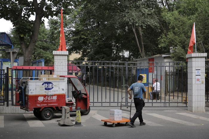 海淀区万柳东路一社区大门封闭，一名快递员将快递车停在大门旁，用小推车将快递运到一旁门卫处寄放。新京报记者 郑新洽 摄