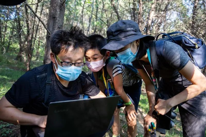 ▲陈雁之（右）和关翔宇（左）、“小虎”（中）正在观看红外相机导出的图像。新京报记者 李凯祥 摄