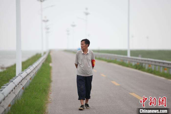 在长长的康山大堤上，一位悬挂“防汛应急”臂章的老人，行走在巡堤的路上。　刘占昆 摄