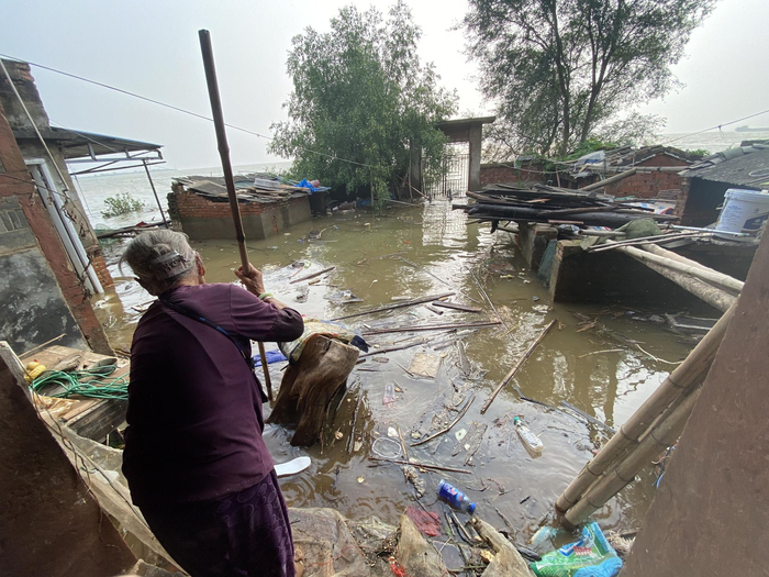 　　村民邹道喜家的平房推开后门仍能看见深深的积水，家里90多岁的老太太也帮忙清理。新京报记者 杜雯雯摄