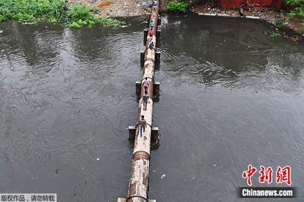 当地时间22日，新德里的人们从一条输水管道上，通过河水泛滥的水渠。